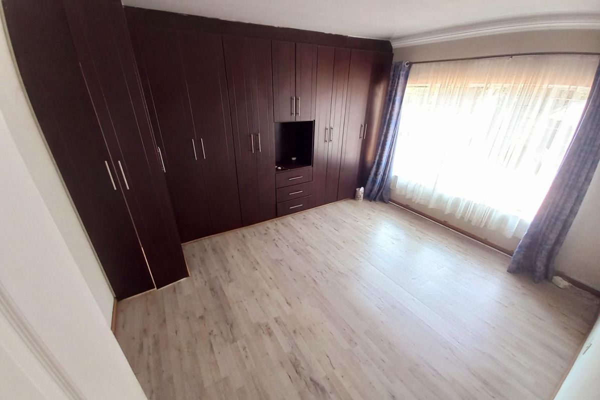 A bright bedroom featuring light-toned laminate flooring and extensive dark wood built-in cabinetry with integrated storage and shelving.