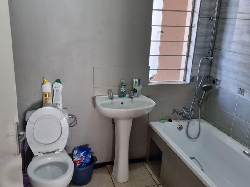 A functional bathroom featuring a pedestal basin, toilet, and bathtub with shower attachment, requiring cosmetic updates to wall finishes and tiling.