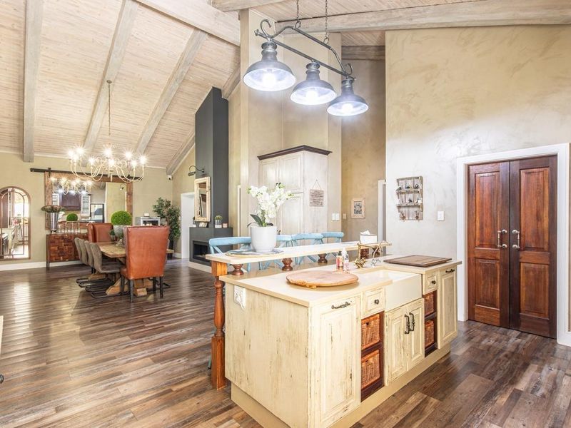 Spacious open-plan living and kitchen area featuring vaulted ceilings with exposed timber beams, a central kitchen island, and a feature fireplace.
