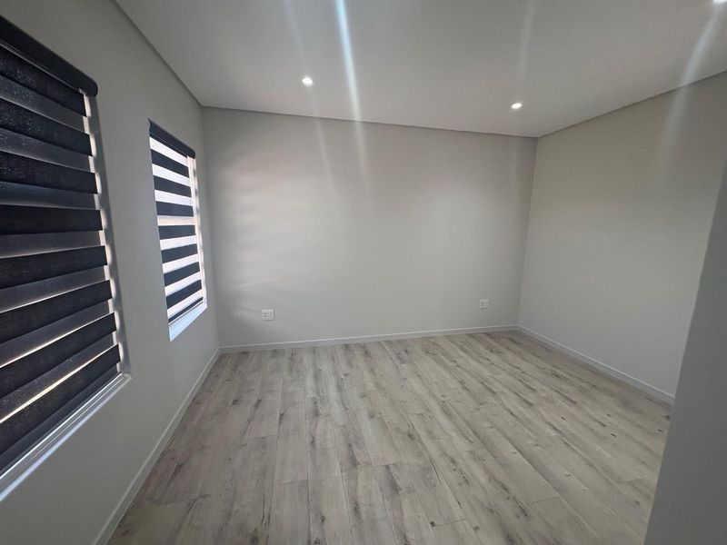 A bright, empty bedroom featuring modern laminate flooring, recessed downlighting, and contemporary zebra blinds, offering a clean and neutral canvas.