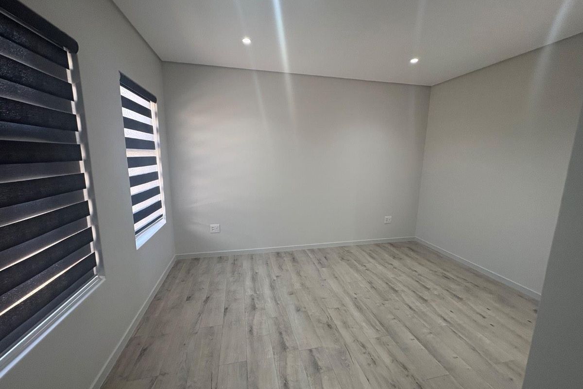 A bright, empty bedroom featuring modern laminate flooring, recessed downlighting, and contemporary zebra blinds, offering a clean and neutral canvas.