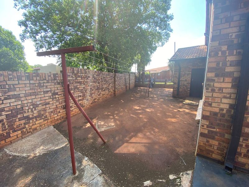A private rear courtyard area featuring face brick boundary walls, an outbuilding, and a paved utility space with a fixed washing line.