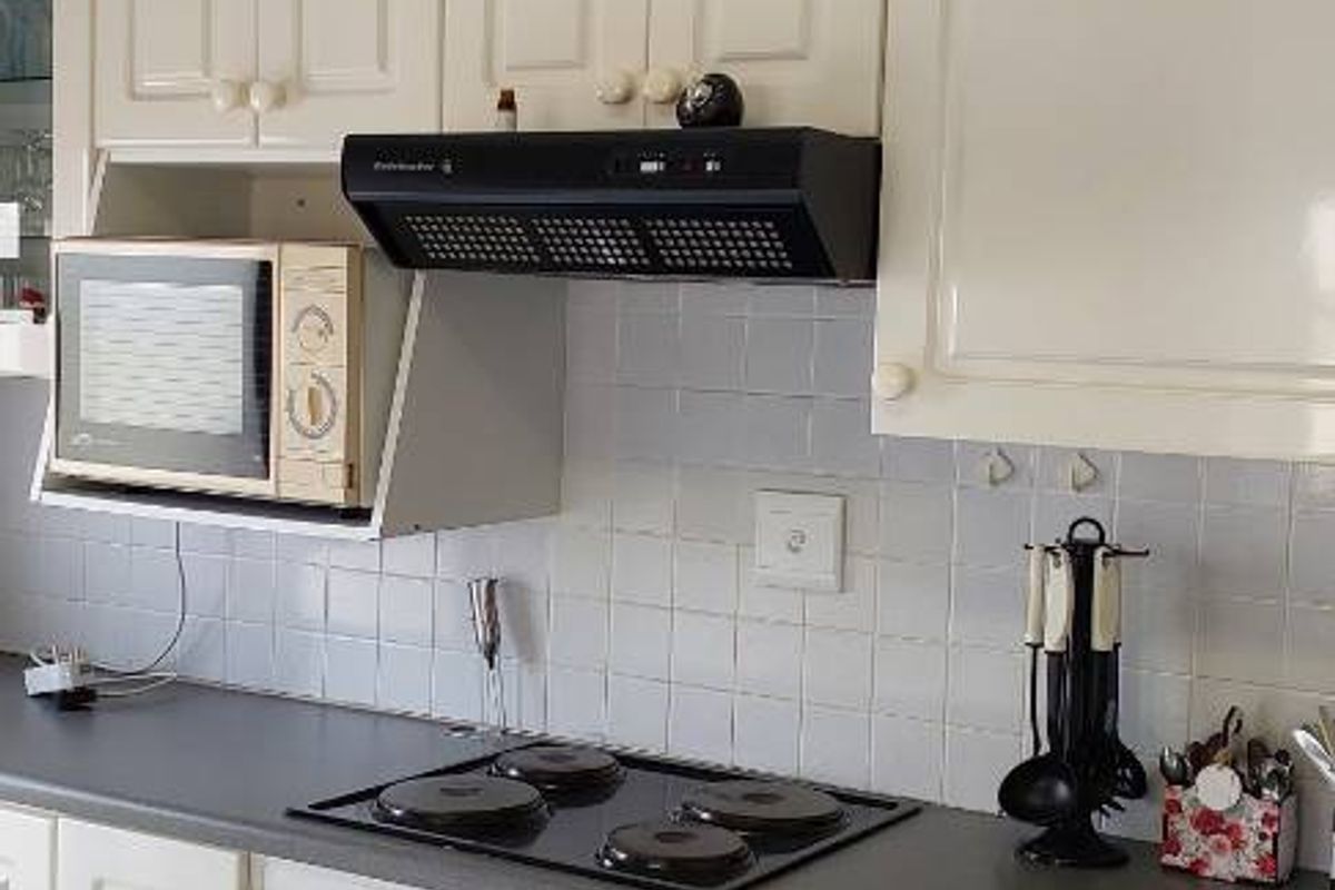 A functional kitchen featuring white cabinetry, a dark countertop, a built-in oven, an electric hob, and an extractor fan with tiled splashbacks.