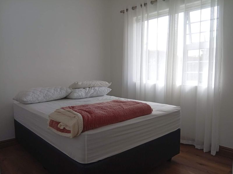 A simple bedroom featuring laminate flooring and a window with sheer curtains, providing a neutral space ready for personalization.