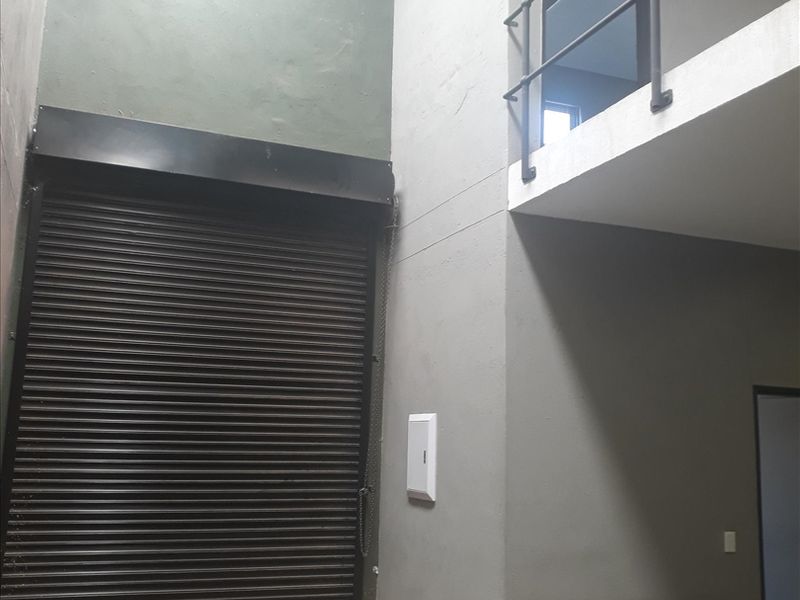 Industrial utility space featuring a high-clearance roller shutter door, concrete flooring, and an elevated mezzanine level with safety railing.