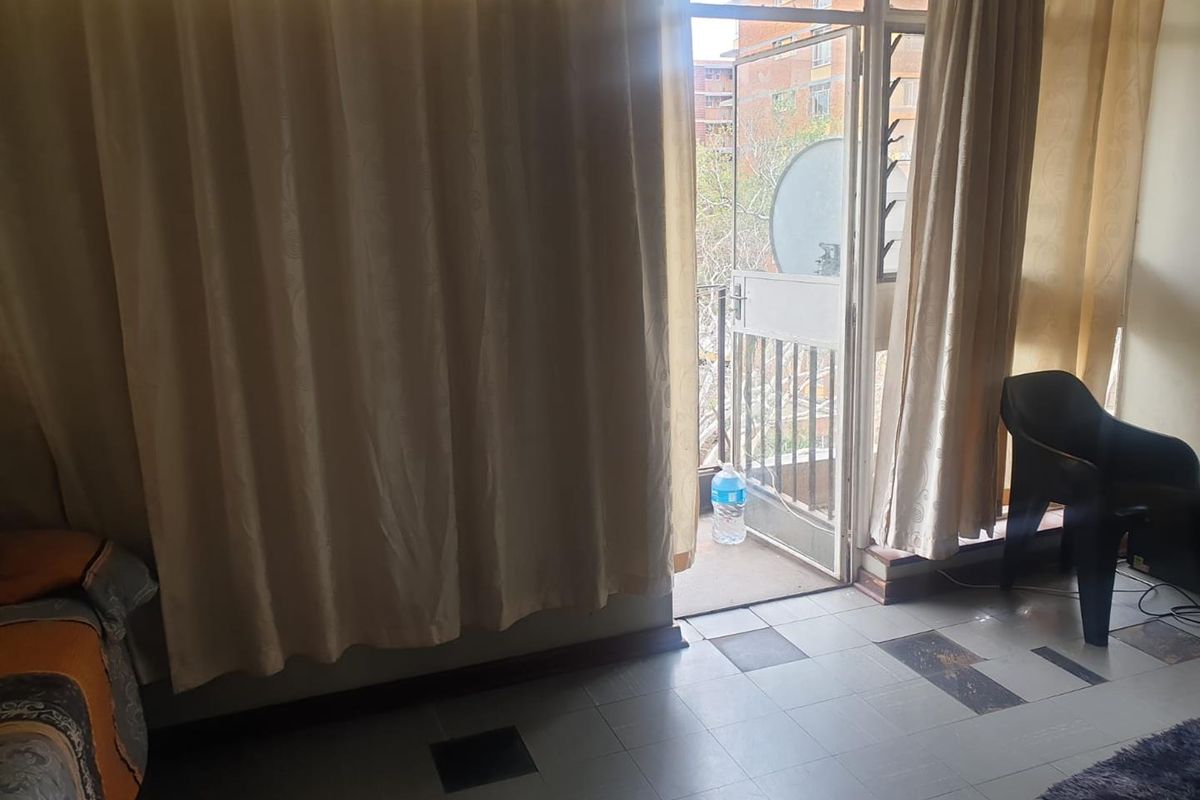 A living area featuring tiled flooring and direct access to a balcony through a glass door, providing natural light and outdoor connectivity.