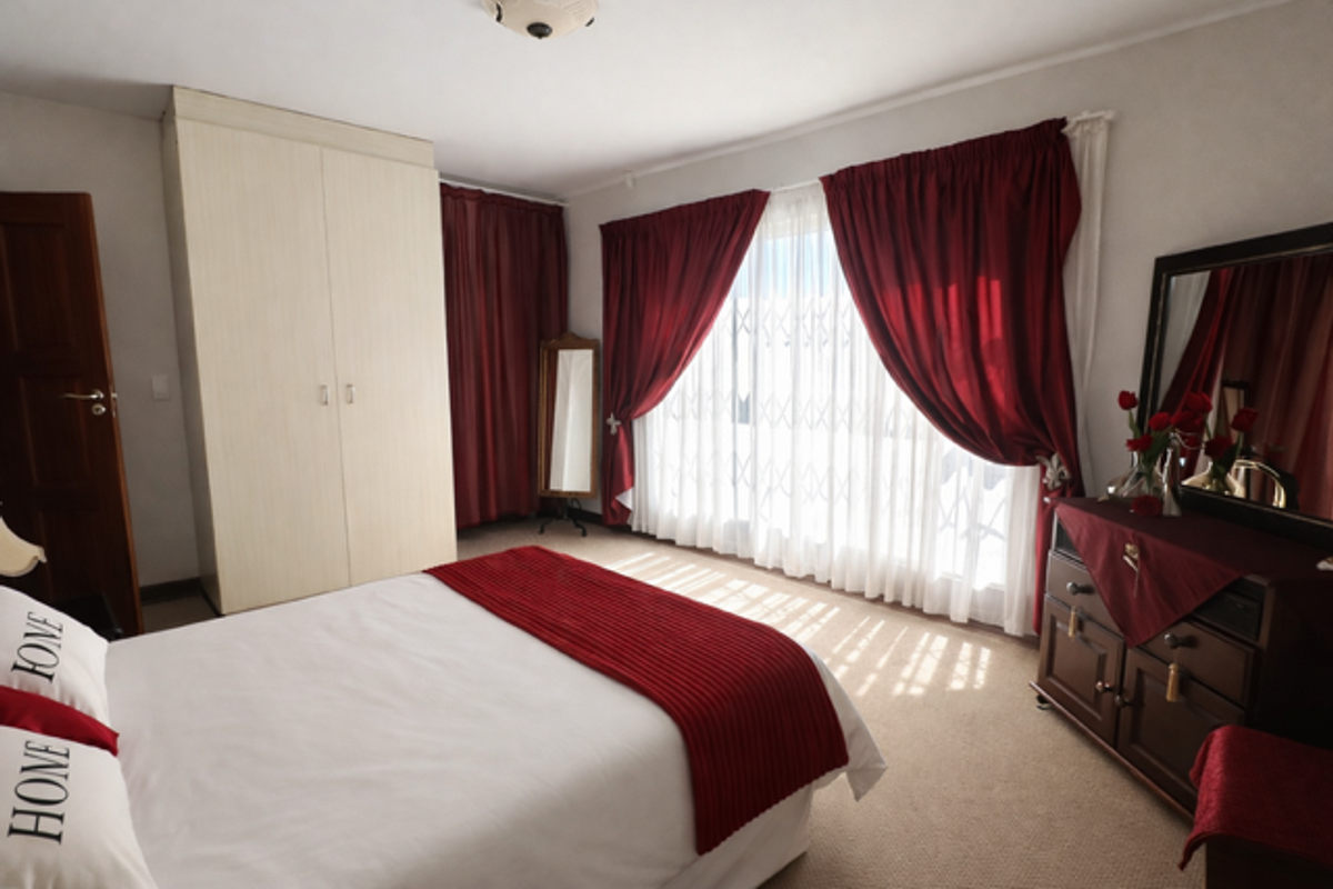 A well-lit bedroom featuring built-in cabinetry, carpeted flooring, and large windows secured with metal security gates.