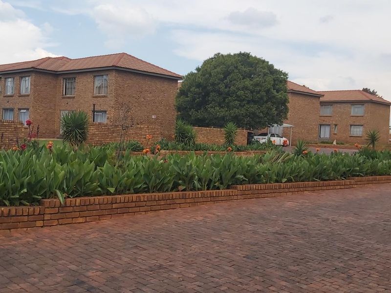 Exterior view of a face-brick apartment complex featuring a paved driveway, landscaped garden beds, and tiled roofing.