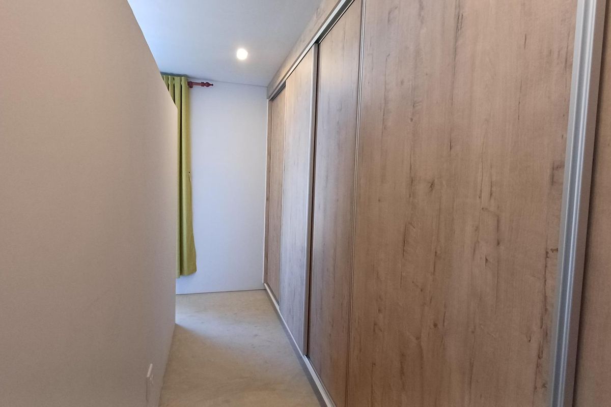 A clean, minimalist bedroom space featuring a large, modern built-in sliding door wardrobe with a wood-grain finish.