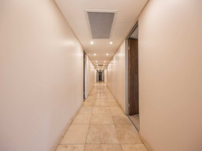 A clean, well-lit office hallway featuring stone tile flooring, recessed ceiling lighting, and integrated HVAC ventilation.