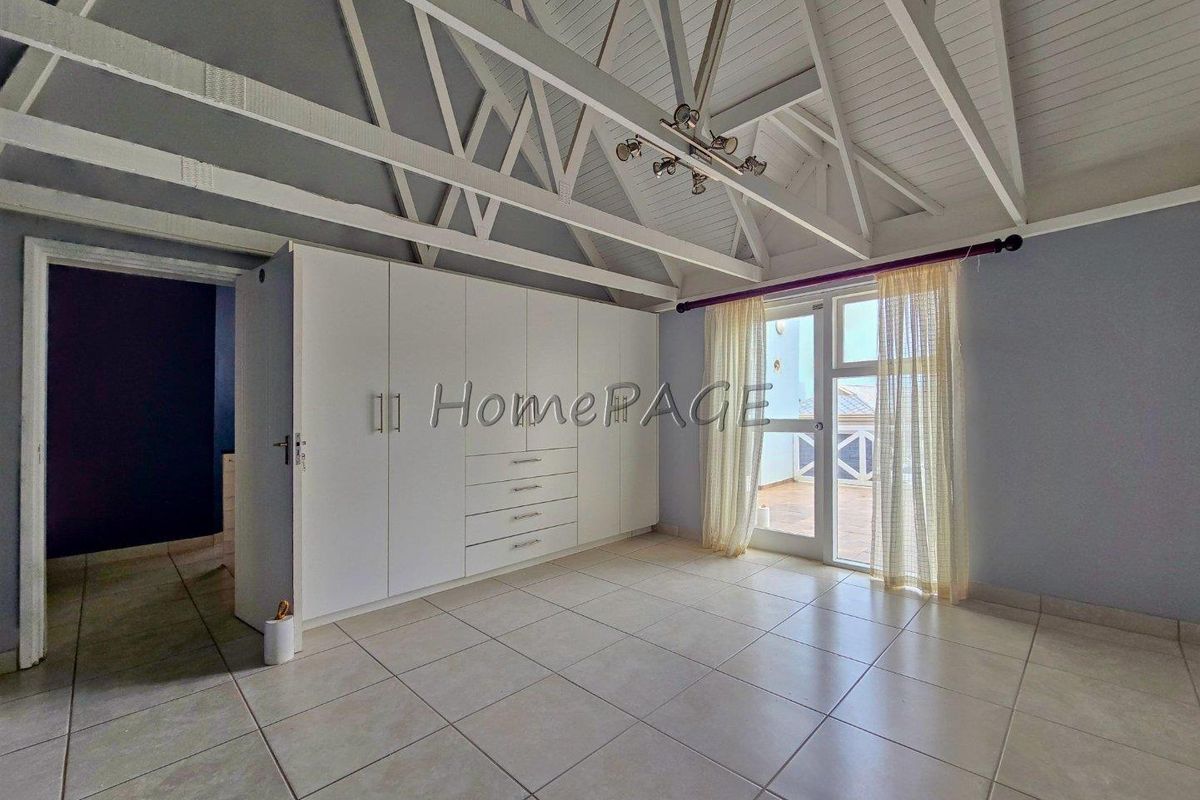 Spacious bedroom featuring a high vaulted ceiling with exposed trusses, built-in cabinetry, tiled flooring, and direct access to an outdoor balcony area.