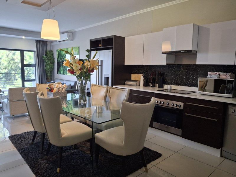 Modern open-plan kitchen and dining area featuring sleek cabinetry, integrated appliances, tiled flooring, and direct access to a balcony through sliding glass doors.