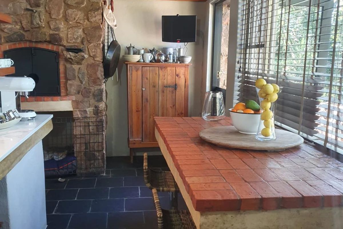 A rustic kitchen area featuring a built-in stone fireplace, tiled breakfast counter, and slate flooring, offering a warm and traditional farm-style atmosphere.