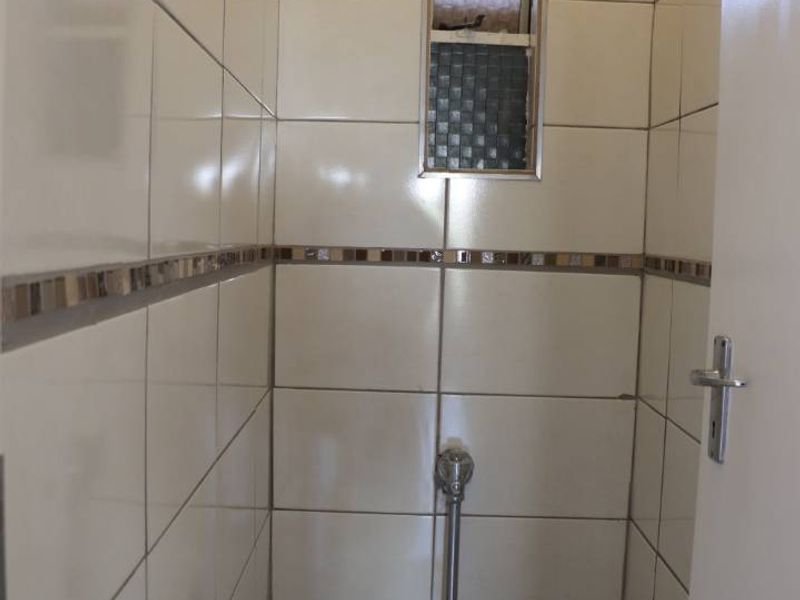 A compact, fully tiled guest bathroom featuring a standard toilet and a vertical window for natural light.