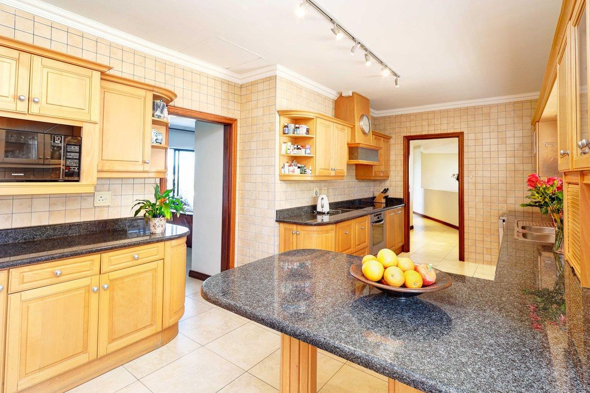 A functional kitchen featuring light wood cabinetry, dark granite countertops, ceramic wall tiling, and integrated appliances, offering a classic and practical layout.