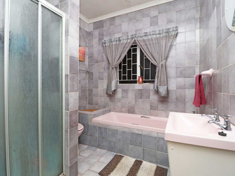 A dated bathroom featuring a pink bathtub and basin, tiled walls, and a separate shower enclosure with security bars on the window.