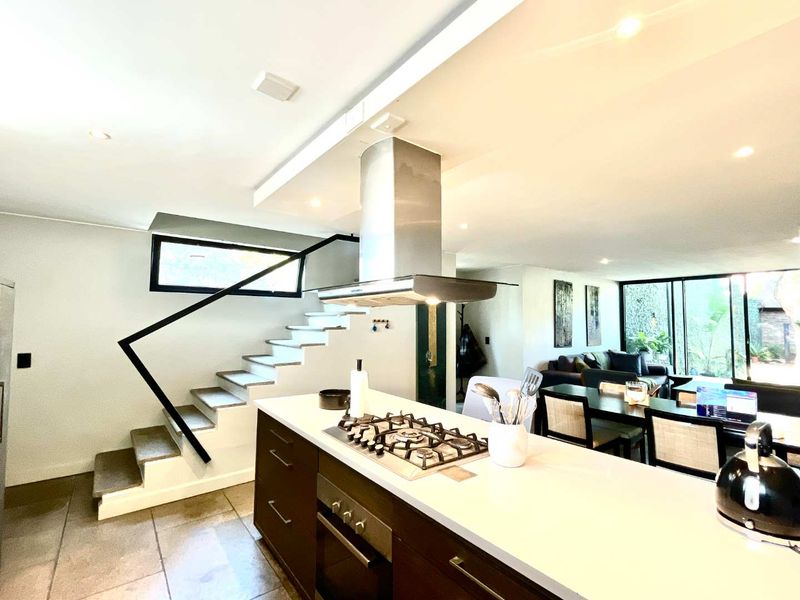 Modern open-plan living area featuring a central kitchen island with gas hob, built-in oven, and a sleek staircase leading to the upper level.