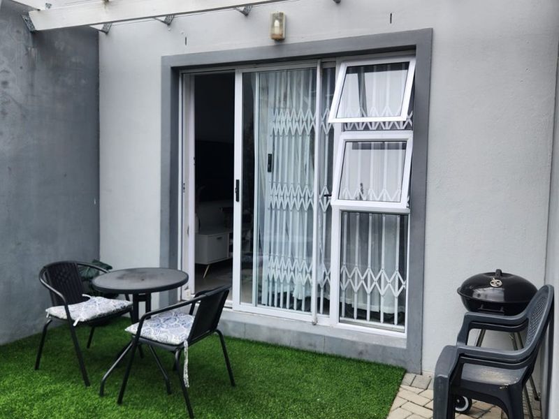 A private patio area featuring paved flooring, artificial grass, a structural awning, and a sliding glass door with security gate access.