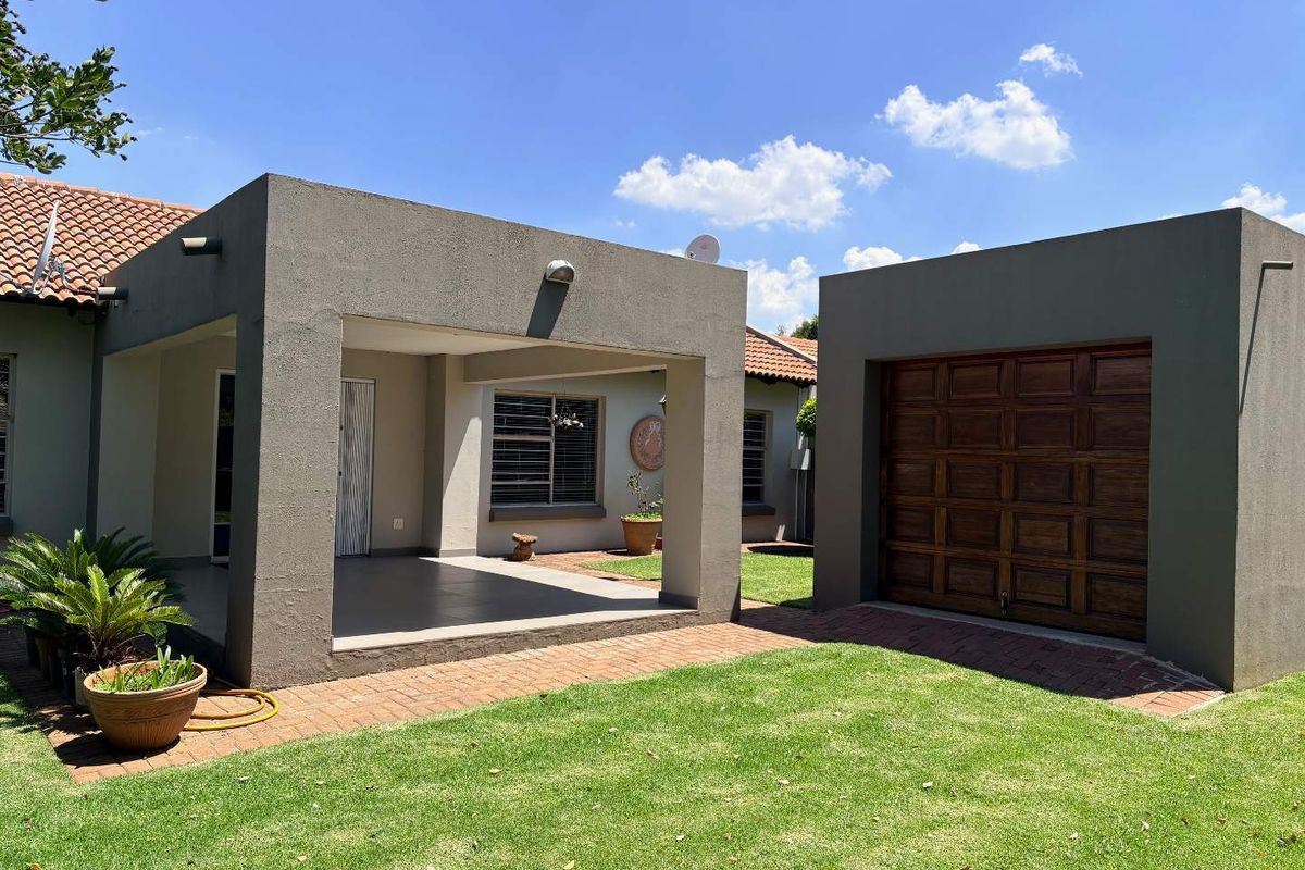 A well-maintained exterior view featuring a covered patio area, a single garage with a wooden door, and a neat garden space.