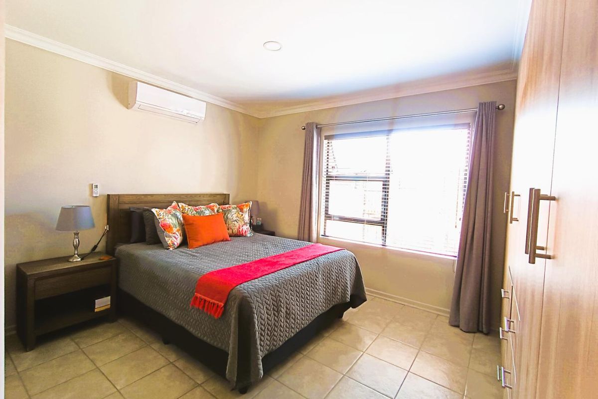 A well-maintained bedroom featuring tiled flooring, built-in wooden cabinetry, and a wall-mounted air conditioning unit.