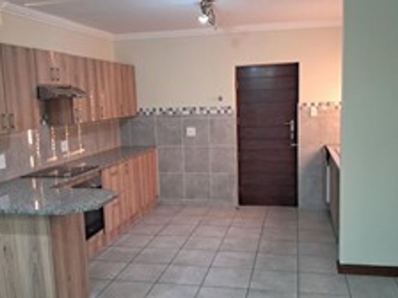 A functional kitchen featuring wood-finish cabinetry, granite countertops, a built-in oven and hob, and neutral tiled flooring throughout.