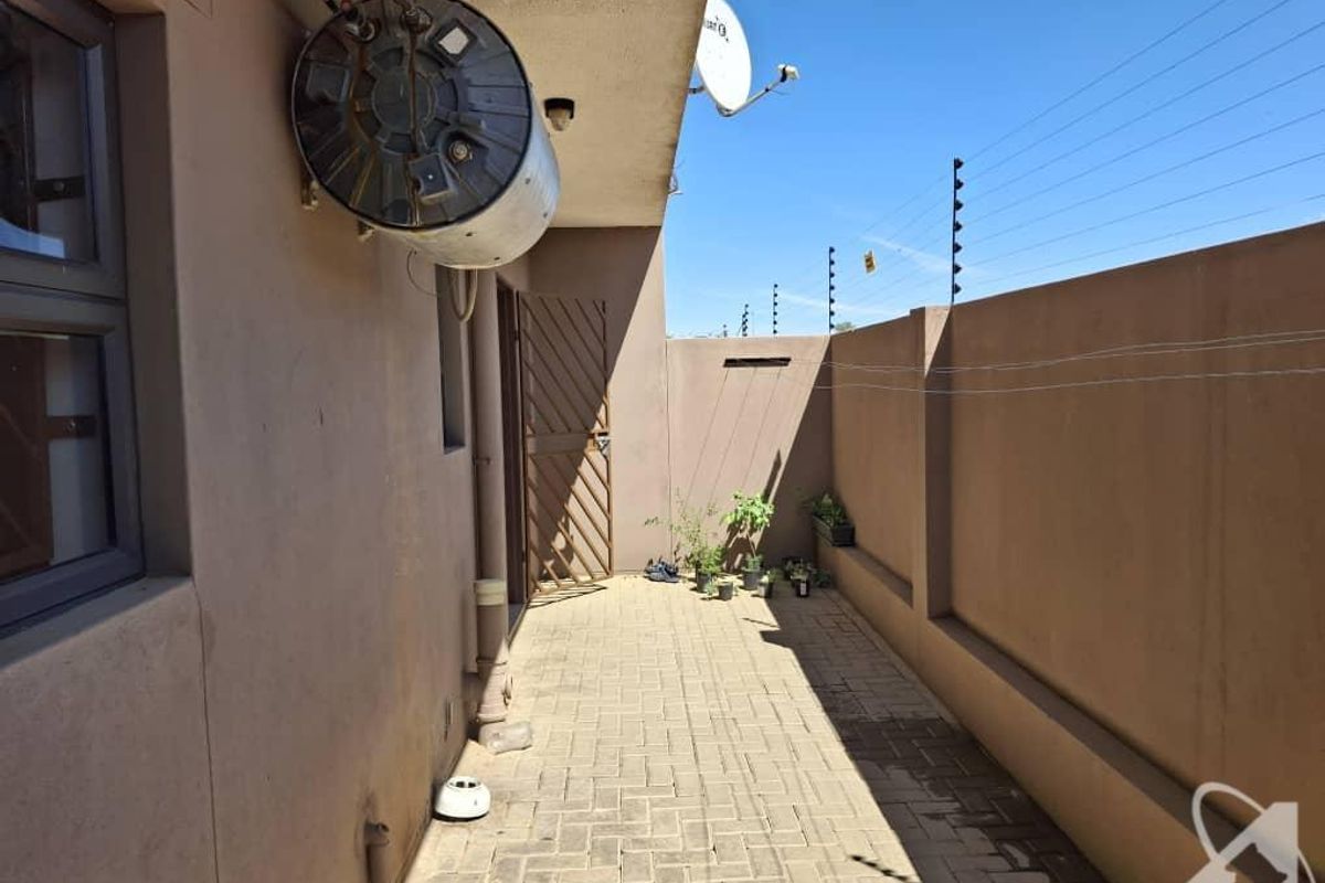 A private rear courtyard featuring paved flooring, a wall-mounted geyser, and secure perimeter electric fencing.