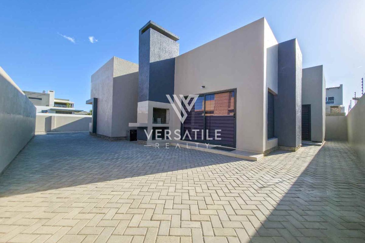 Modern rear exterior view featuring paved courtyard, built-in braai area, and sliding glass doors leading into the home.