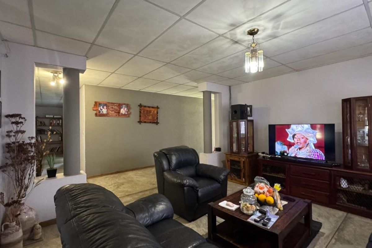 A living room featuring a drop ceiling, structural columns, and a central pendant light fixture, offering a functional space with potential for modernization.