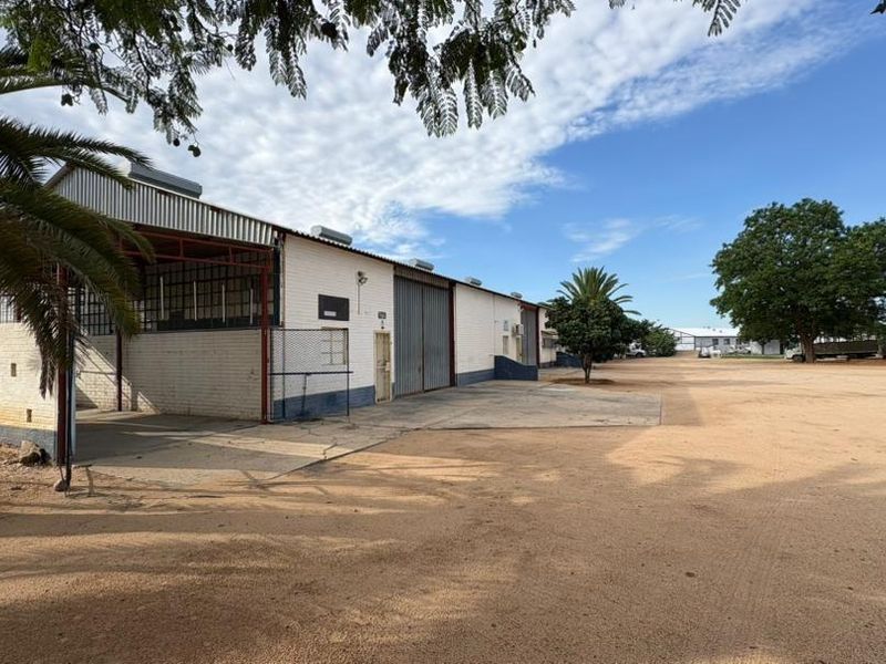 Exterior view of a commercial warehouse facility featuring a large open yard, metal roofing, and a covered loading area.