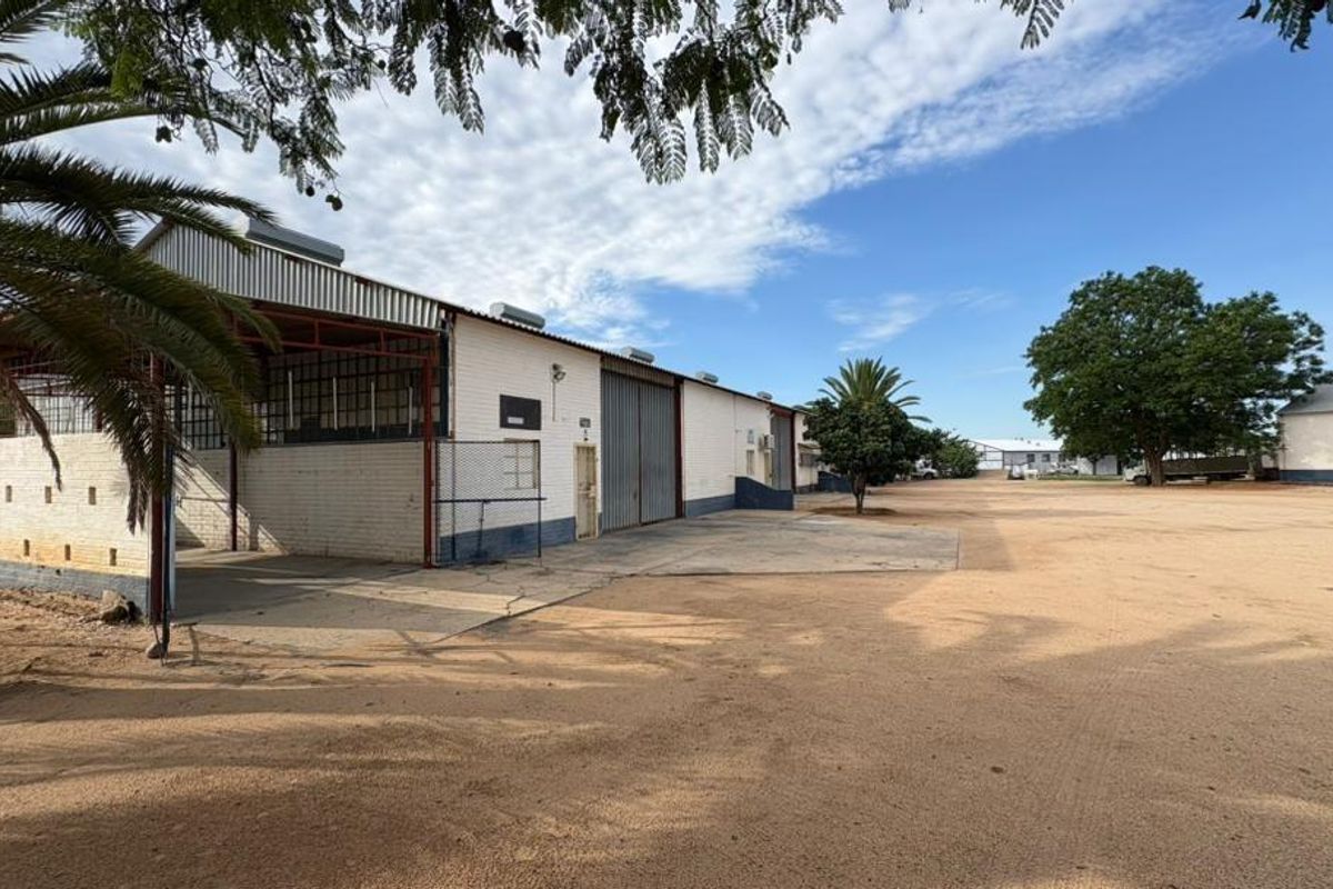 Exterior view of a commercial warehouse facility featuring a large open yard, metal roofing, and a covered loading area.