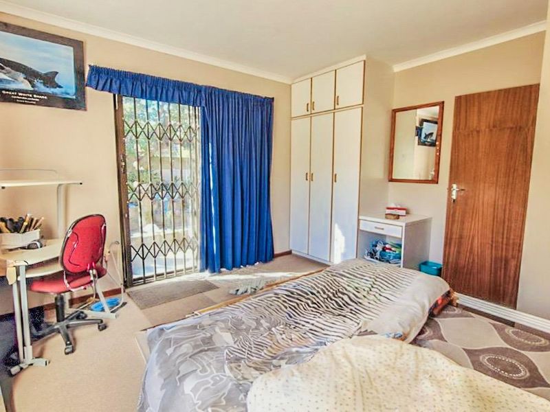 A functional bedroom featuring built-in cupboards, a sliding door with a security gate, and neutral wall finishes.