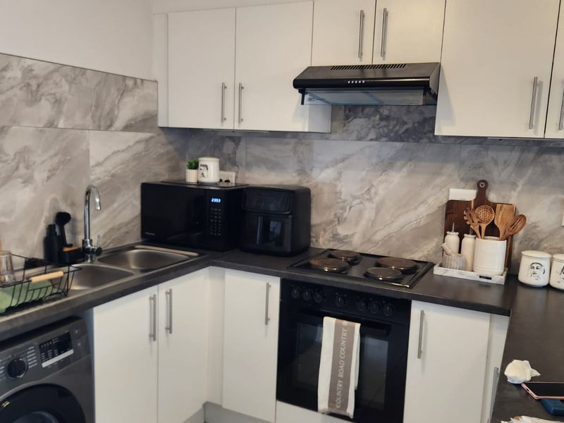 A functional kitchen featuring white cabinetry, marble-look splashback, built-in oven with electric hob, extractor fan, and tiled flooring.