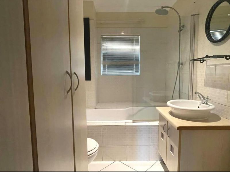 A functional bathroom featuring a shower-over-bath combination, a vessel sink vanity, and built-in storage cupboards with tiled finishes throughout.