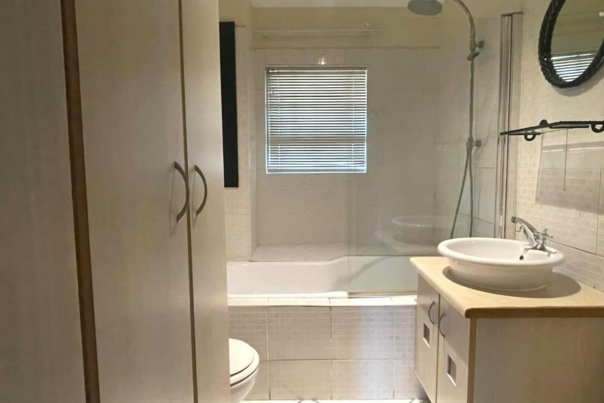 A functional bathroom featuring a shower-over-bath combination, a vessel sink vanity, and built-in storage cupboards with tiled finishes throughout.