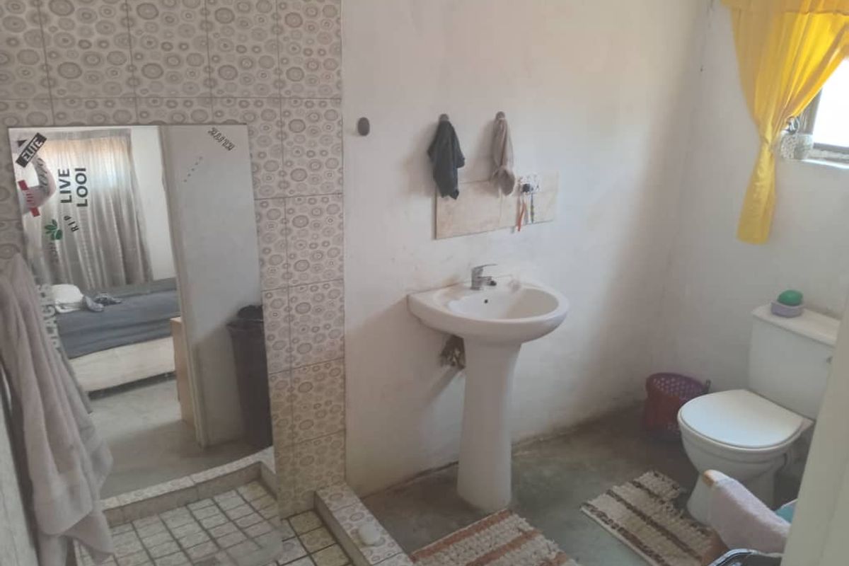A functional bathroom featuring a pedestal basin, standard toilet, and tiled wall accents, requiring cosmetic updates to improve the overall finish.