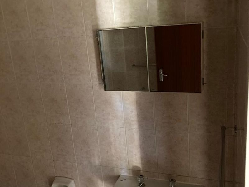 A functional bathroom featuring a pedestal basin, wall-mounted medicine cabinet, and tiled walls, currently in need of cosmetic updates.