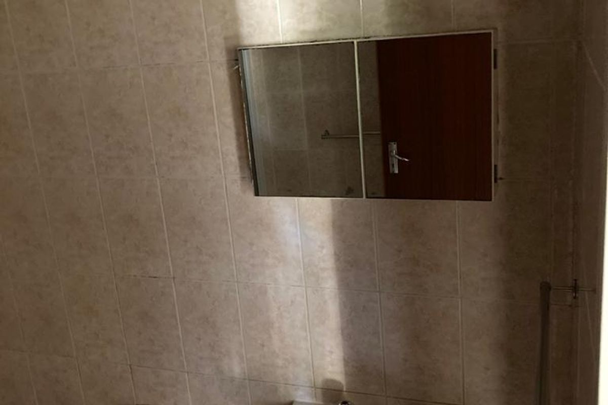 A functional bathroom featuring a pedestal basin, wall-mounted medicine cabinet, and tiled walls, currently in need of cosmetic updates.