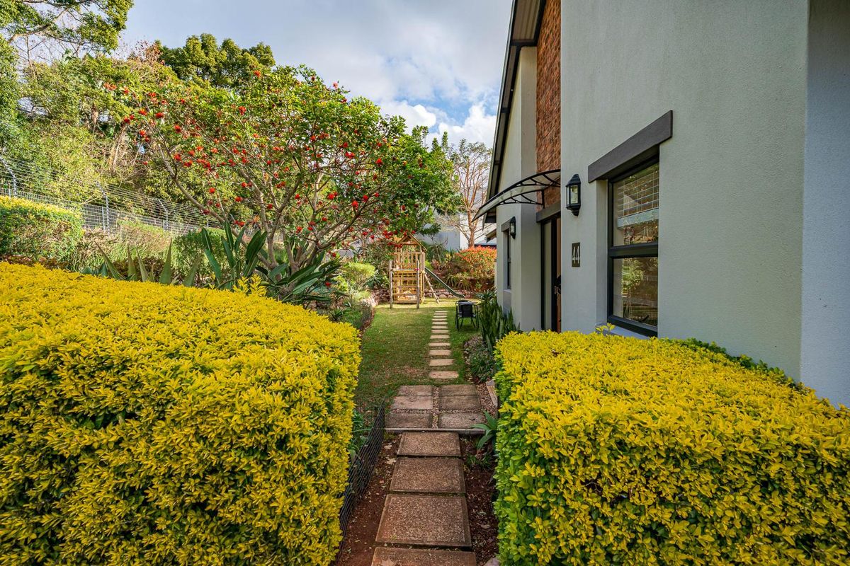 A well-maintained rear garden area featuring a paved walkway, established landscaping, and a brick and rendered exterior facade.