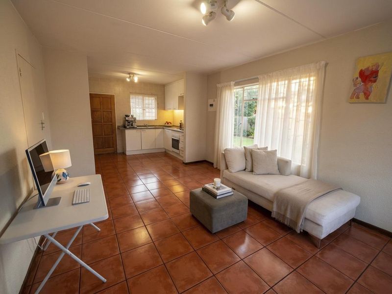 Open-plan living area featuring ceramic tile flooring, a functional kitchen with built-in cabinetry and appliances, and direct access to the garden via sliding doors.