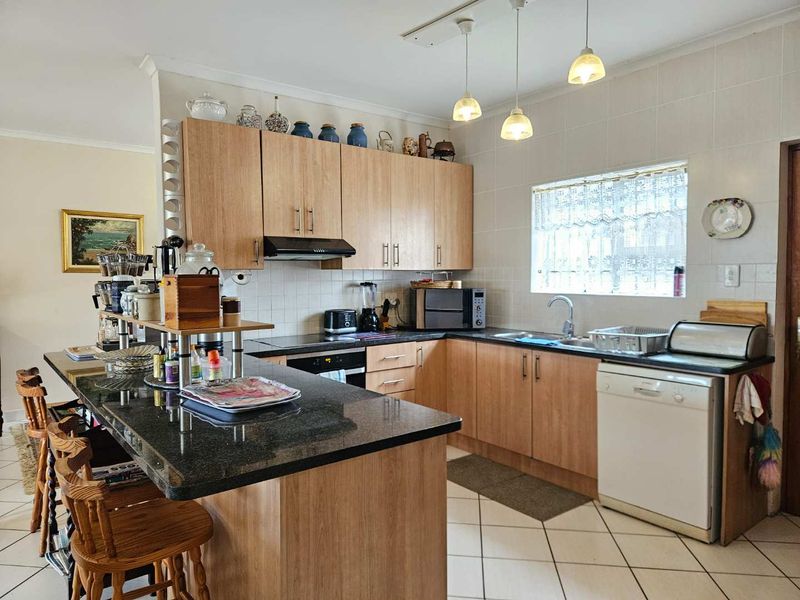 A functional kitchen featuring light wood cabinetry, dark granite countertops, a tiled backsplash, and a breakfast bar island with pendant lighting.