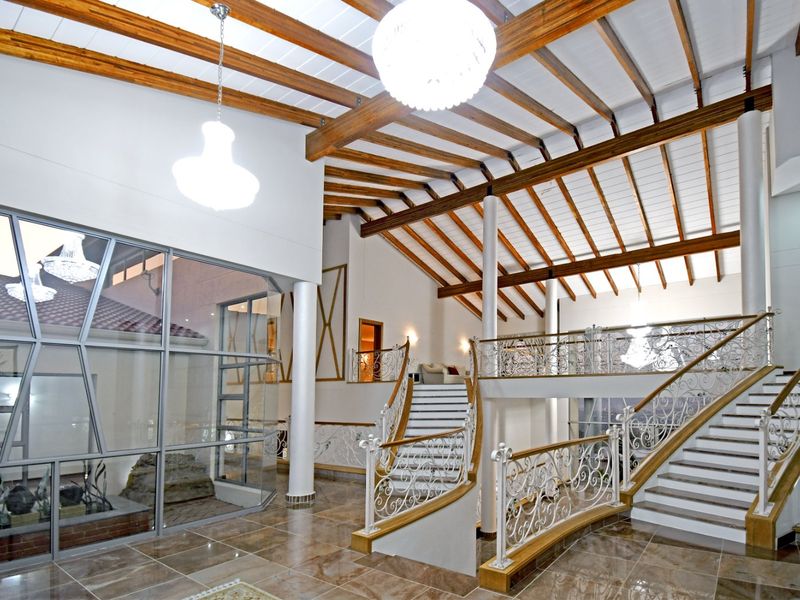 Spacious grand entrance hall featuring a double staircase, exposed timber ceiling beams, and large glass windows providing an airy, open atmosphere.