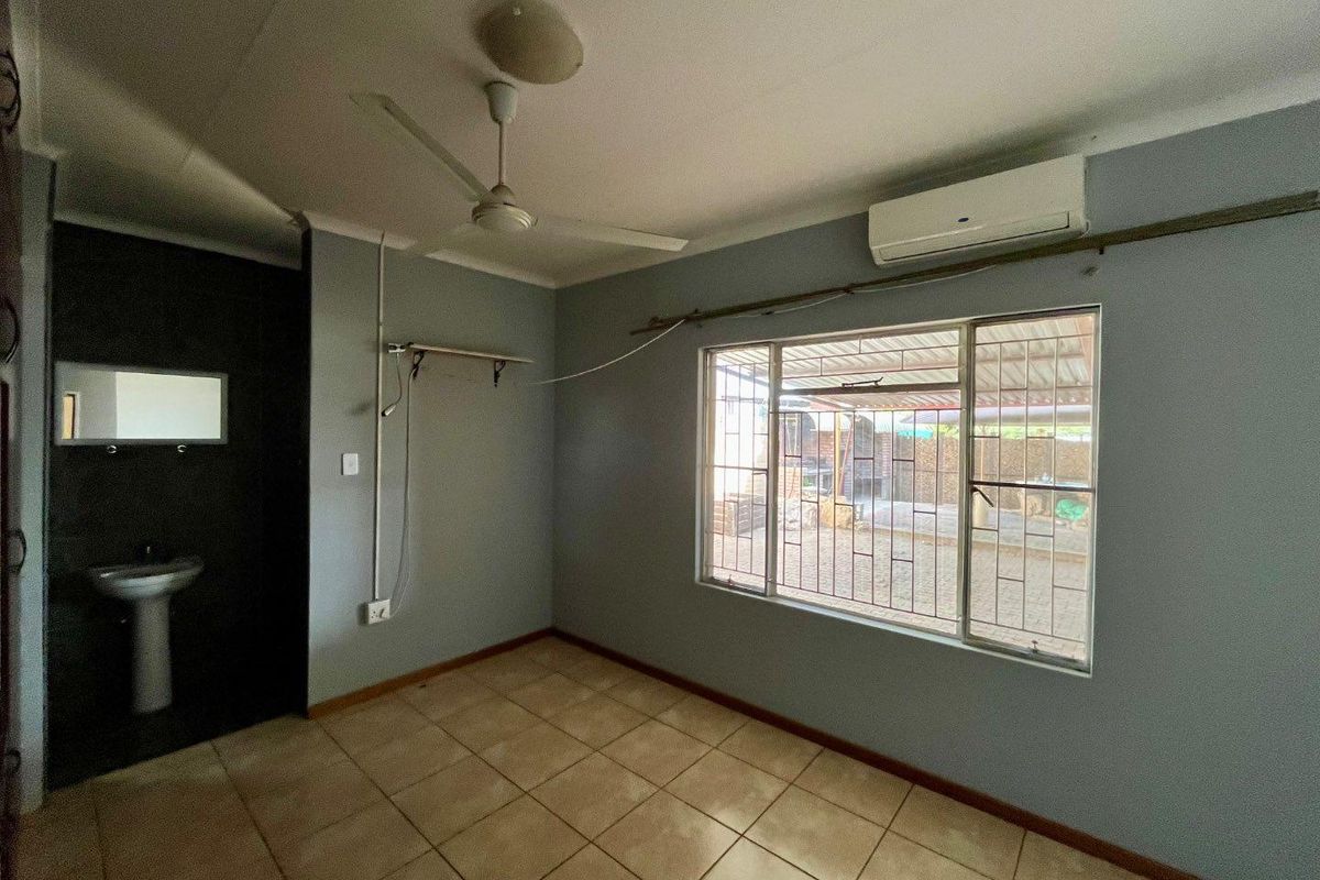 A functional bedroom featuring tiled flooring, a ceiling fan, wall-mounted air conditioning unit, and a small integrated vanity area with a pedestal sink.