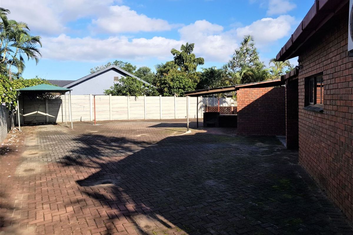 Spacious rear courtyard featuring extensive brick paving, a covered patio area with a built-in braai, and secure perimeter walling.
