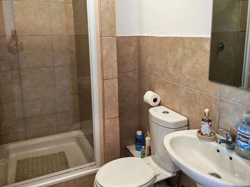 A functional bathroom featuring a shower enclosure, pedestal basin, and toilet with neutral wall tiling.