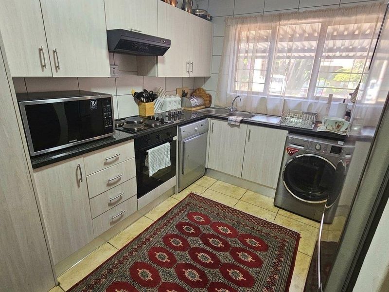 A functional kitchen featuring light-toned cabinetry, dark laminate countertops, a built-in oven with hob, and tiled finishes throughout.