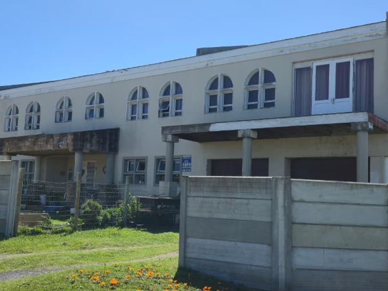 A double-storey residential property featuring arched windows and a balcony, enclosed by a precast concrete boundary wall.