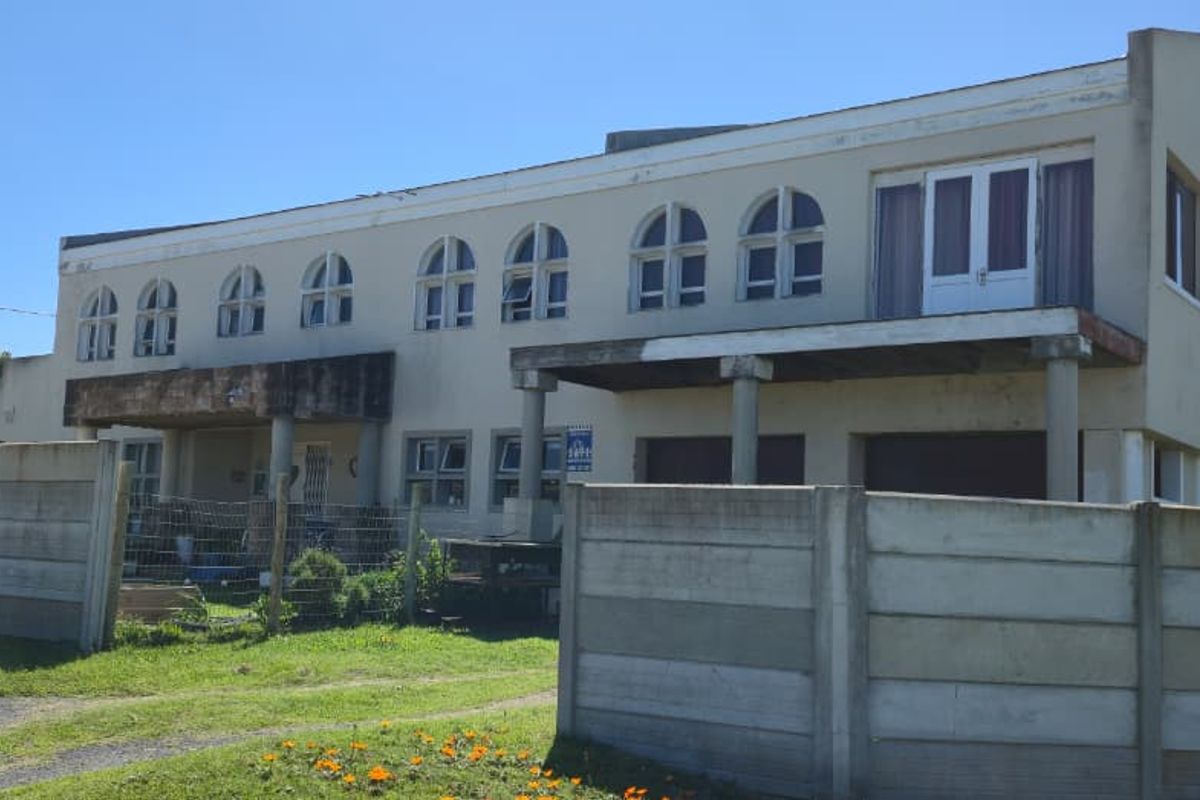 A double-storey residential property featuring arched windows and a balcony, enclosed by a precast concrete boundary wall.