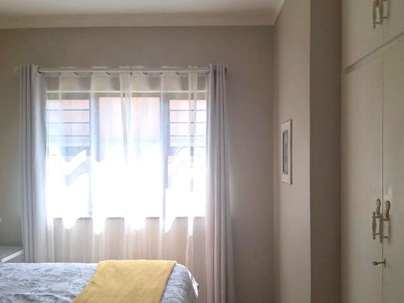 A bedroom featuring built-in cupboards, tiled flooring, and a window with security bars, providing a functional and neutral living space.