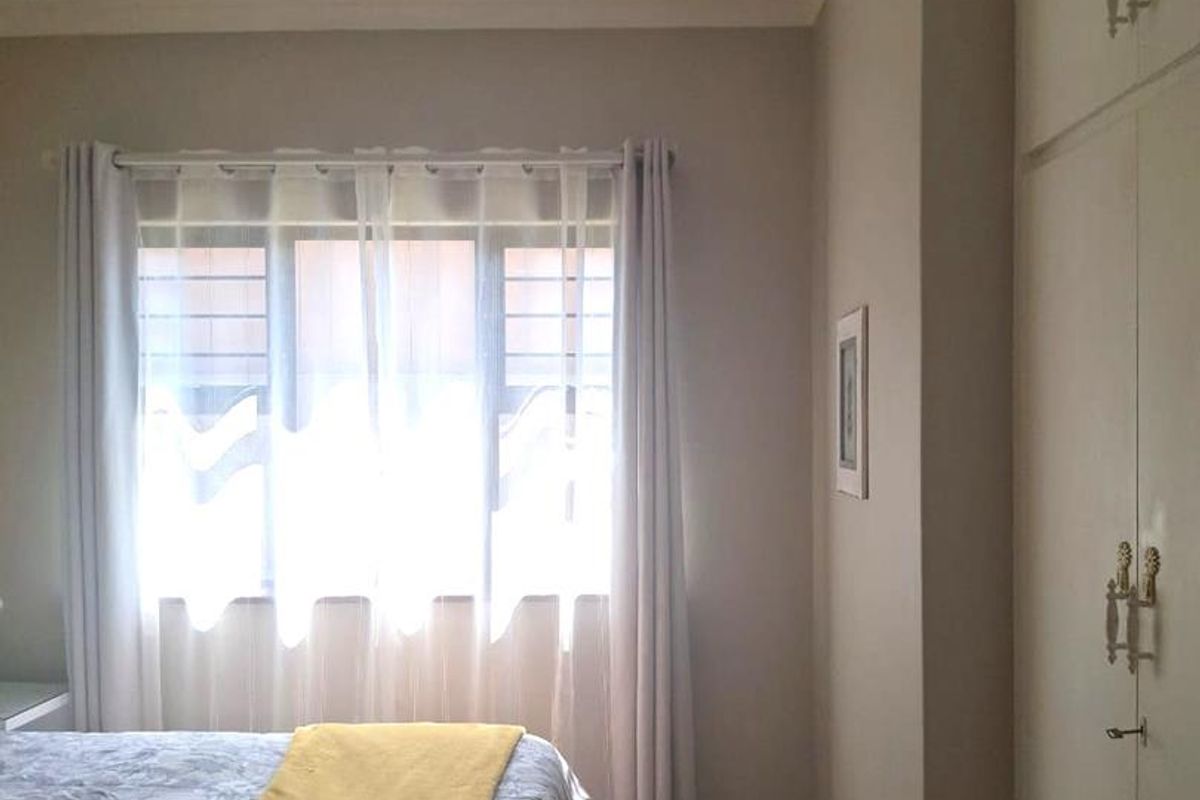 A bedroom featuring built-in cupboards, tiled flooring, and a window with security bars, providing a functional and neutral living space.