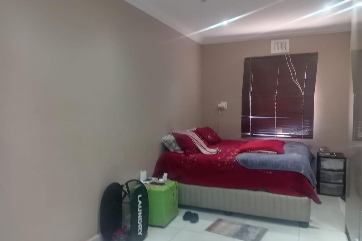 A bedroom featuring tiled flooring, built-in cupboards, and venetian blinds, providing a functional space with neutral wall tones.